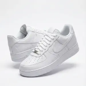Tenis blancos de caña baja con textura reptil, perforaciones en puntera, suela gruesa y detalles de la marca.